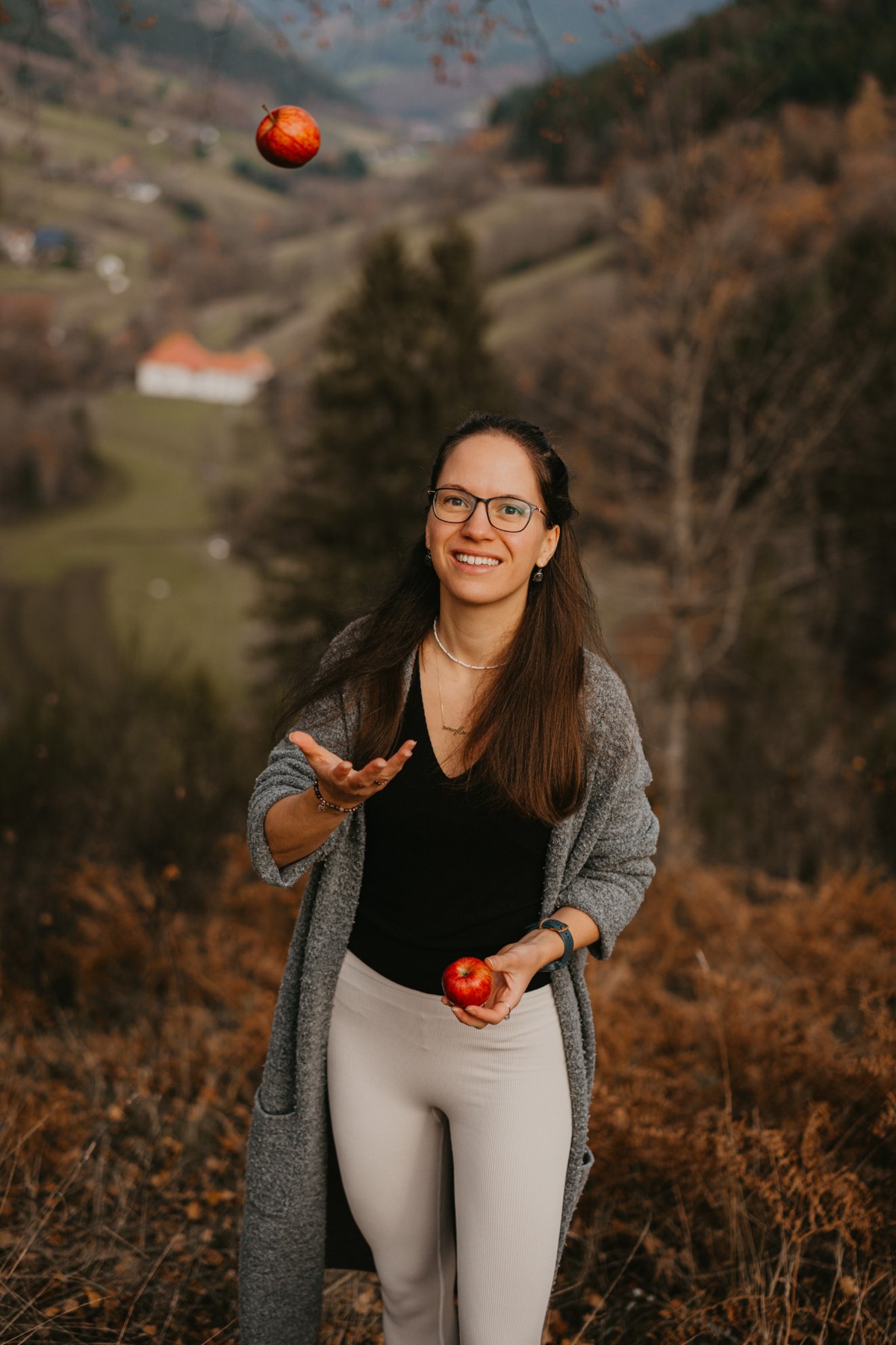 Kim lächelt in der Natur und wirft einen roten Apfel in die Luft
