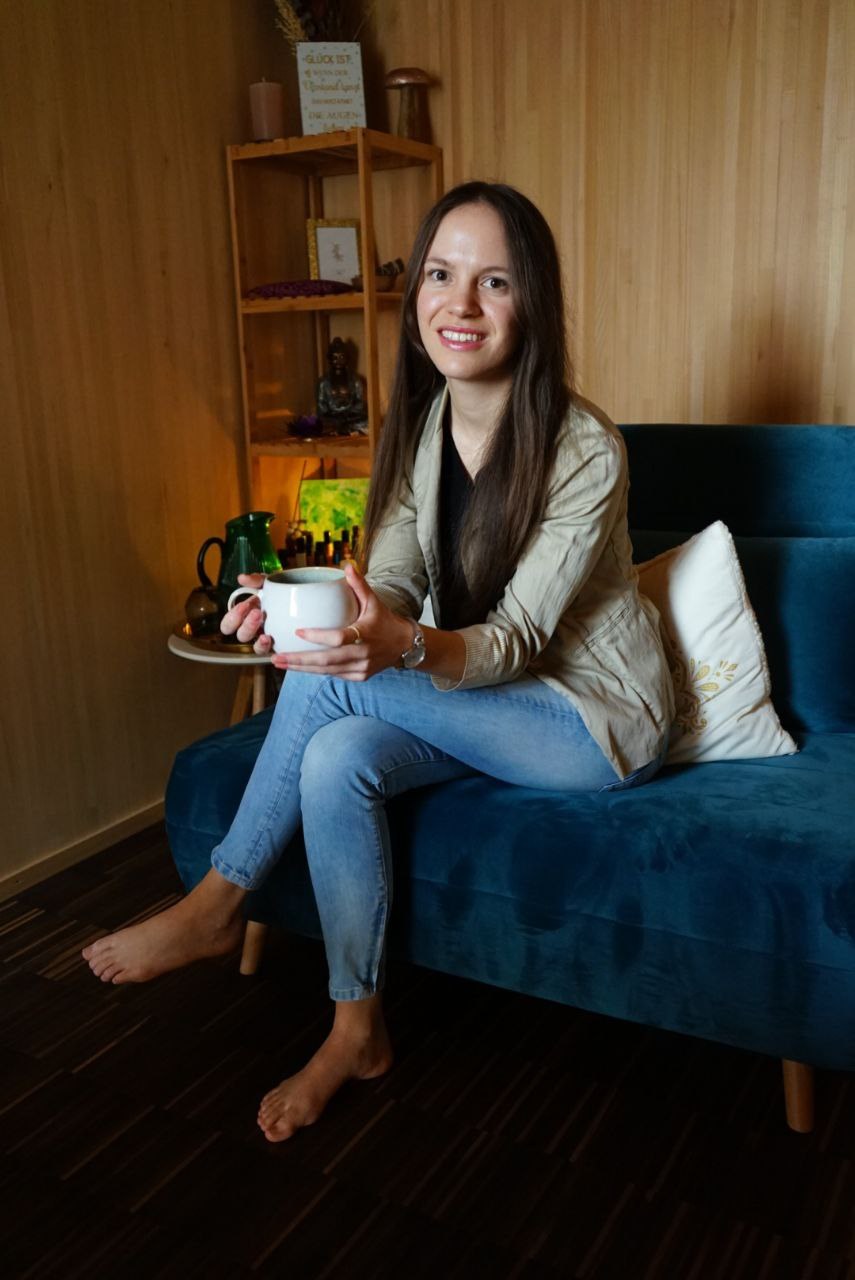 Kim lächelt mit einer Tasse auf dem blauen Sofa